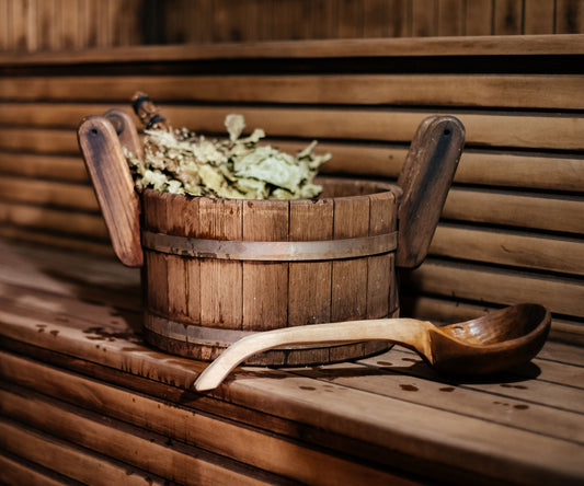 Holzkübel mit Birkenzweigen und Saunakelle auf einer Saunabank