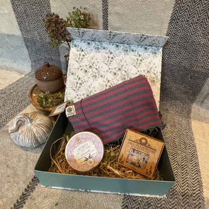 Geschenkbox mit Eukalyptus-Muster, gefüllt mit einem Hamamtuch, Peelingsalz und Badesalz, dekorativ auf Holzwolle arrangiert.