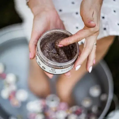 Hand entnimmt VEGAN FOX Kaffee-Körperpeeling über einem Fußbad